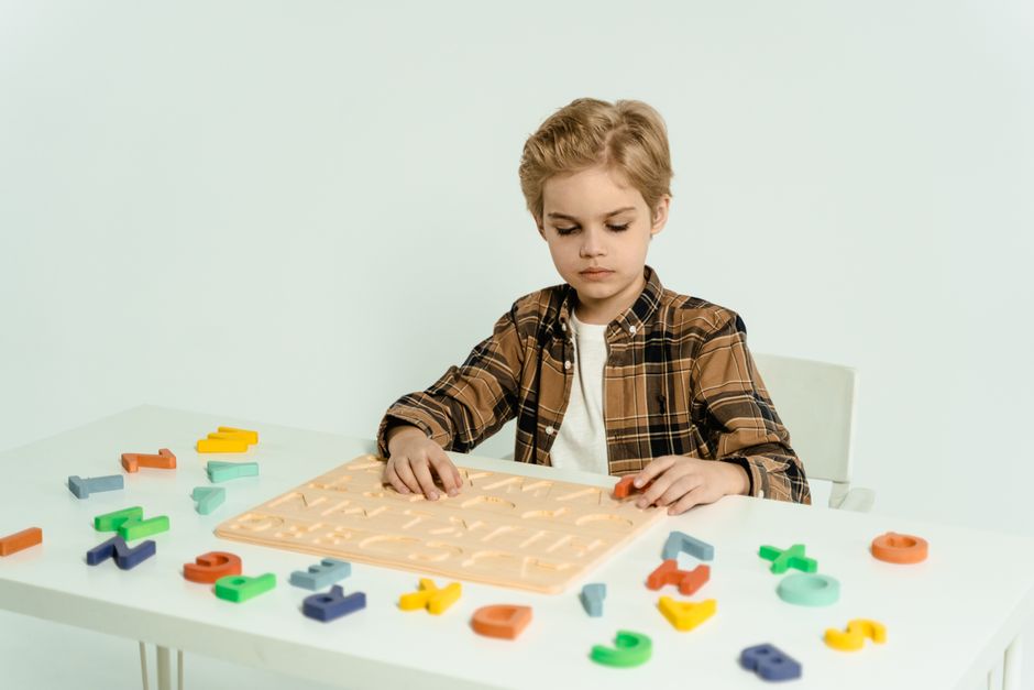 Blonde child engaging with educational alphabet toys at a table indoors.