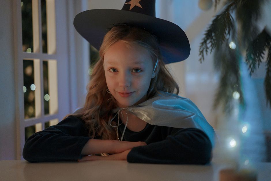 Enchanting young girl dressed as a wizard, sitting near window with magical ambiance.
