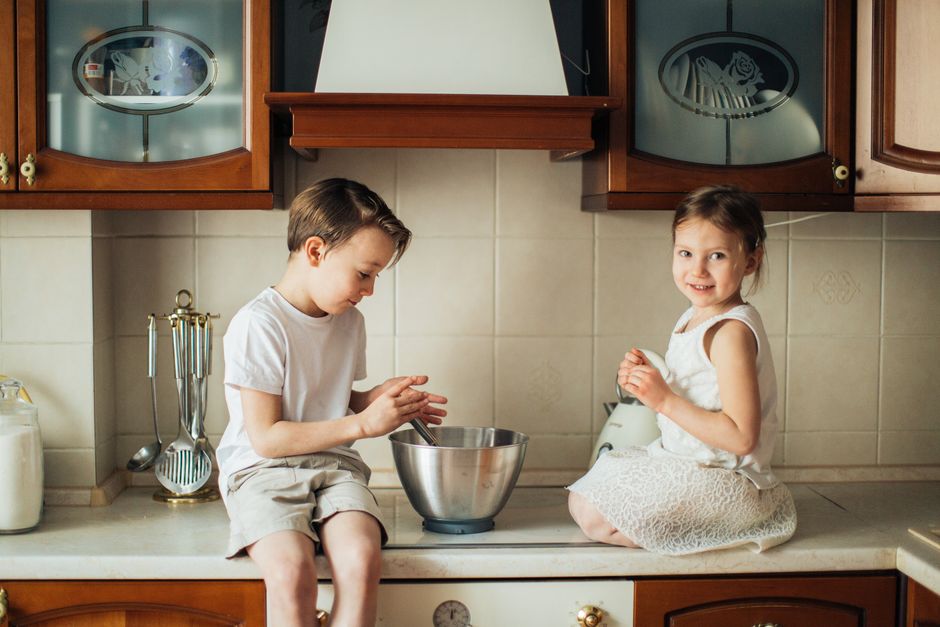 Two children enjoy baking together on a kitchen counter, creating joyful childhood memories.