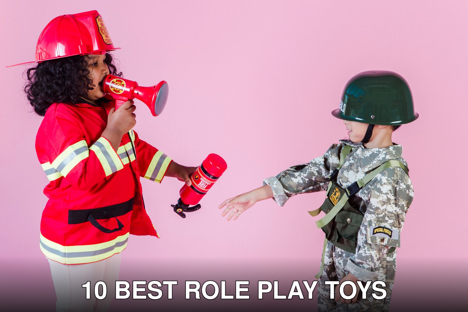 Side view of multiracial children in military uniform and fireman costume with megaphone and fire extinguisher standing together on pink background in helmets