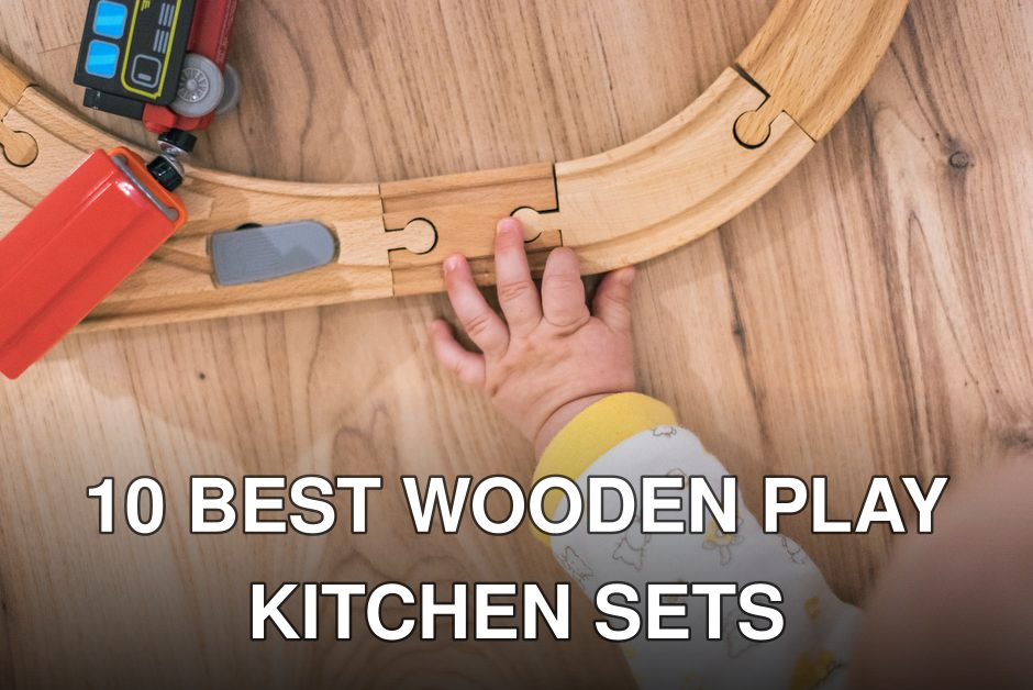 A toddler's hand assembling a wooden toy train track on a hardwood floor.