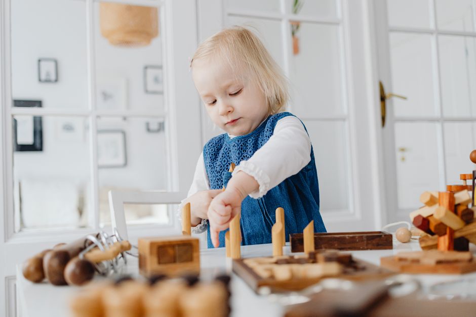Blonde toddler focused on assembling wooden toys indoors, enhancing creativity.