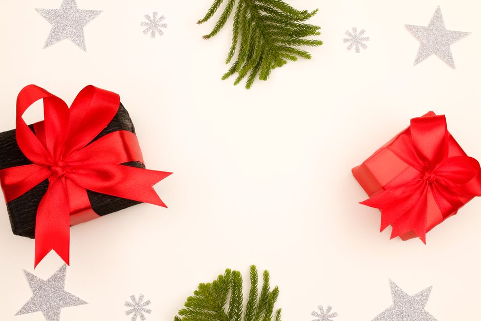 Elegant Christmas gift boxes with red bows and pine sprigs on a flat lay background.