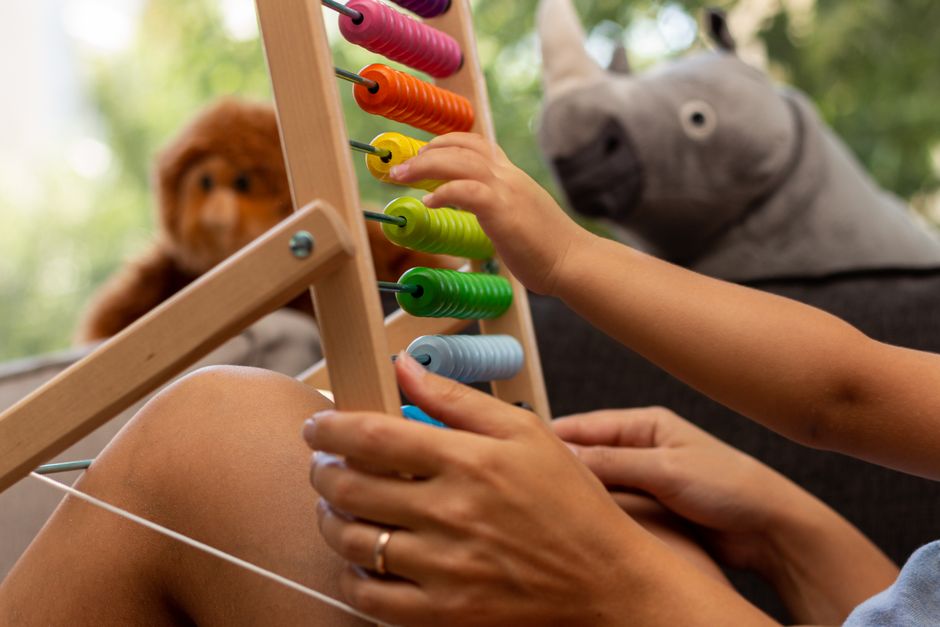 Child's hand playing with a colorful wooden abacus, enhancing early math skills in a playful home setting.