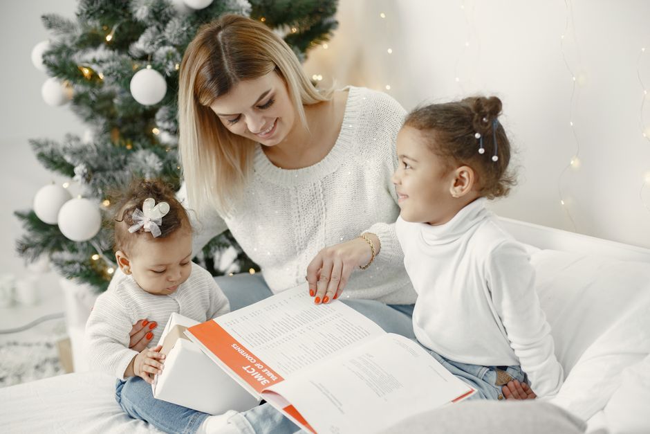 A joyful family moment with a mother and daughters reading together near a Christmas tree.