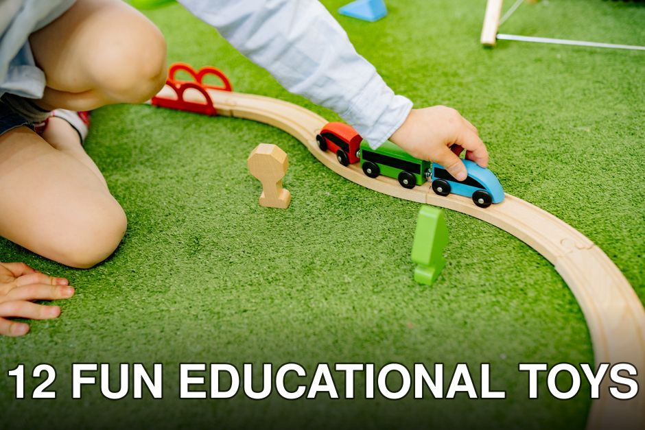 A young child plays with a colorful wooden toy train set on green grass.