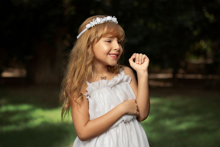 A smiling girl in a white dress enjoying a sunny day outdoors.