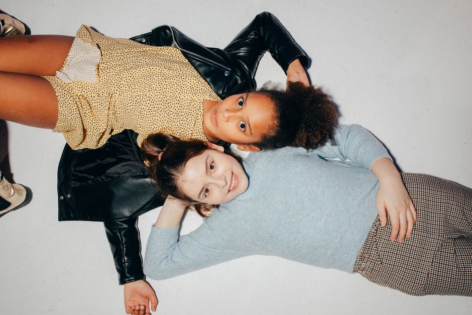 Two girls lying on a white background, showcasing their joyful friendship.