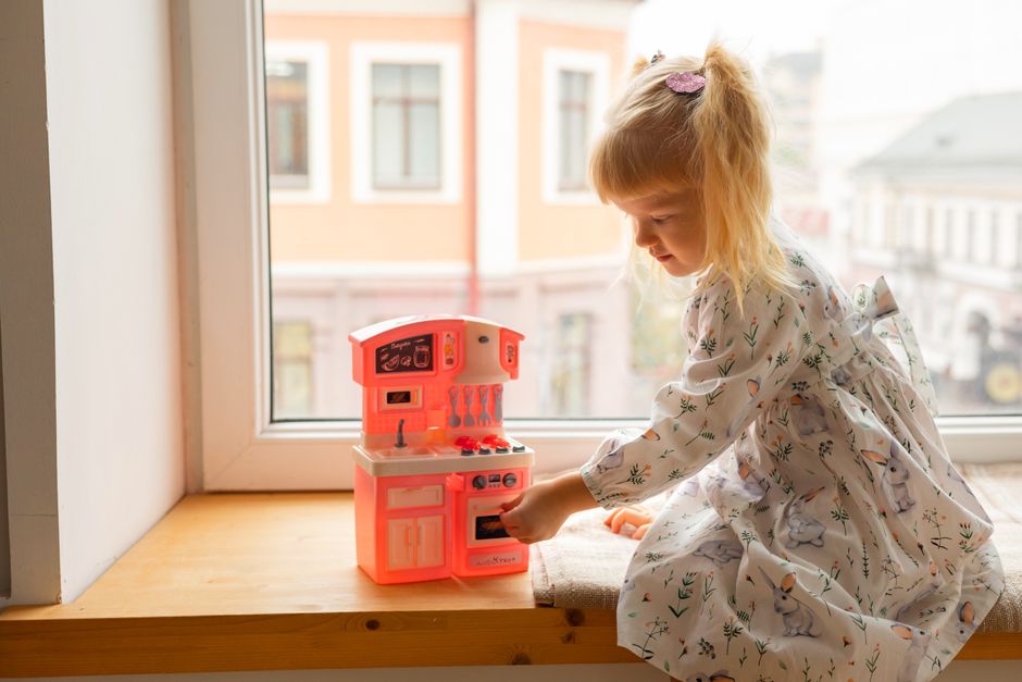 Young girl in a floral dress playing with a toy kitchen set on a sunny day.