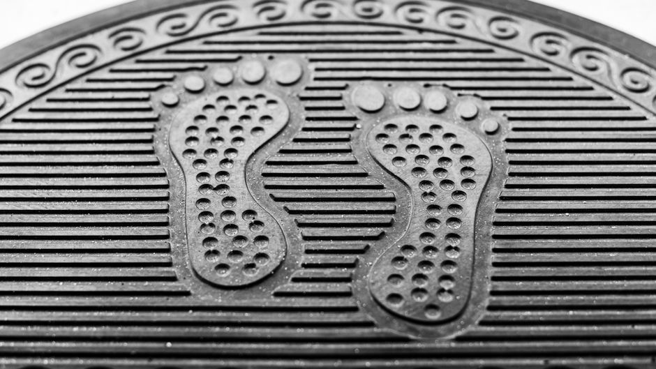 Close-up of a textured black rubber doormat with a footprint design. Ideal for home or office use.