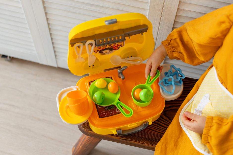 A child playing with a toy kitchen set, engaging in creative pretend play indoors.