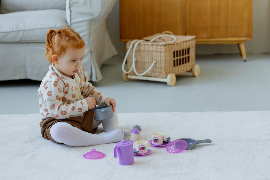 Adorable toddler enjoying time with a colorful outdoor tea set inside a cozy home environment.