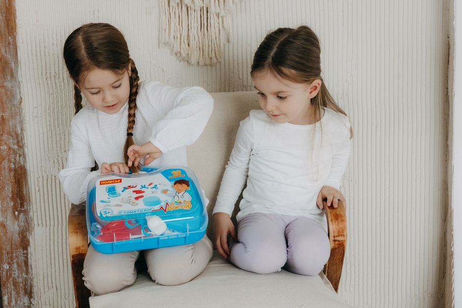 Two young girls play with a toy doctor kit indoors, showcasing curiosity and fun.