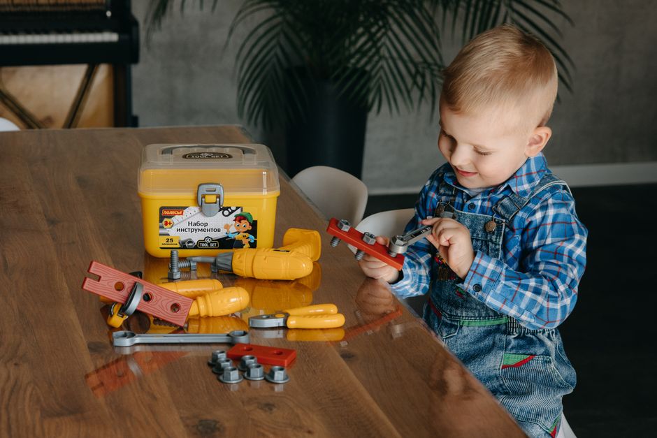 Young boy joyfully plays with toy tools at home, fostering creativity and learning through play.