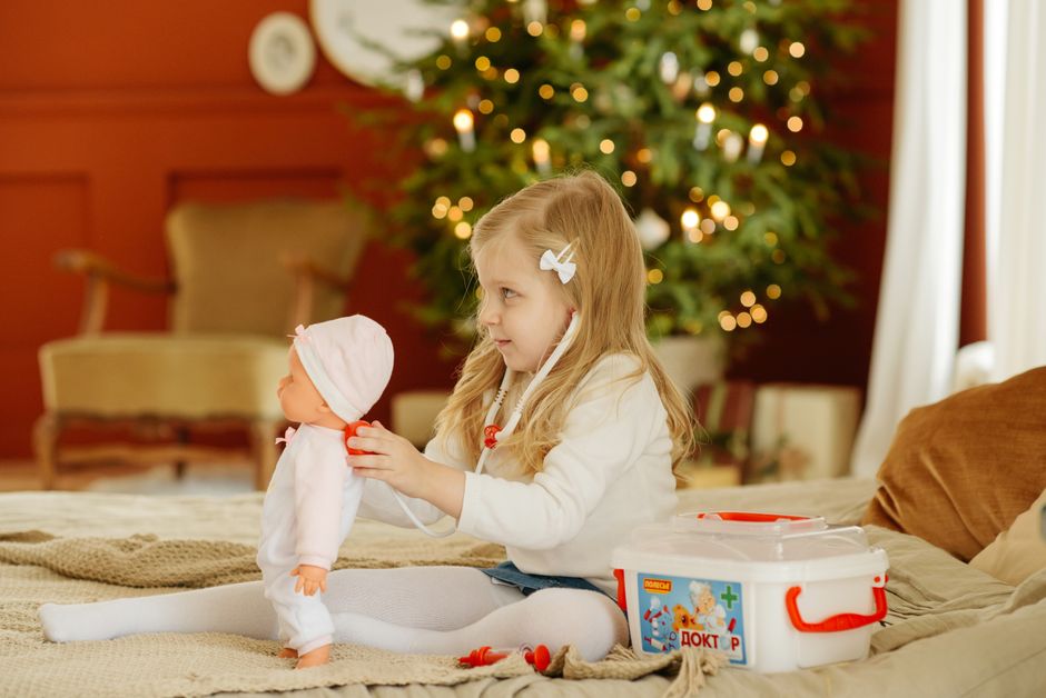A young girl plays doctor with her doll near a Christmas tree, showcasing imaginative play and holiday spirit.