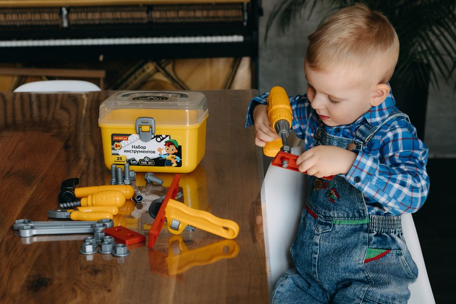 A young boy engaged in creative play with a colorful toy tool set at a table indoors.