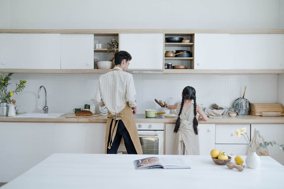 A father and daughter preparing food in a modern kitchen setting.