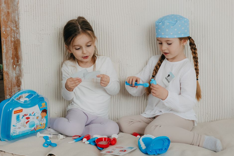Two young girls playing dentist with toy kit indoors, promoting imaginative play.