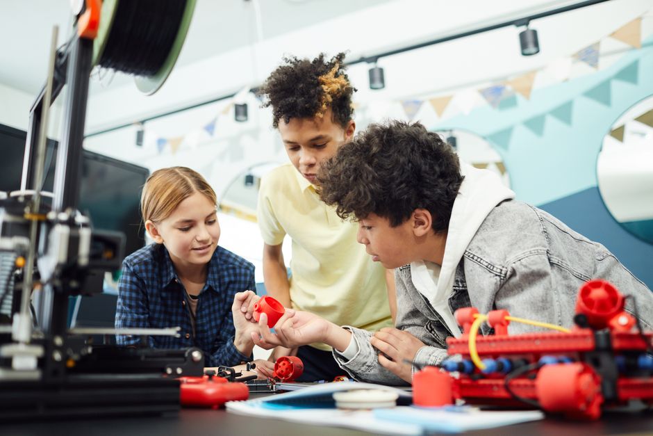 Concentrated group of children sitting at table and exploring new engineering device together in light room