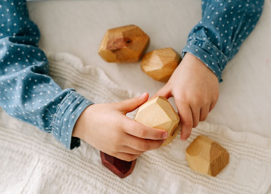 Close-up of a child's hands playing with wooden geometric blocks, highlighting mindfulness and creativity.