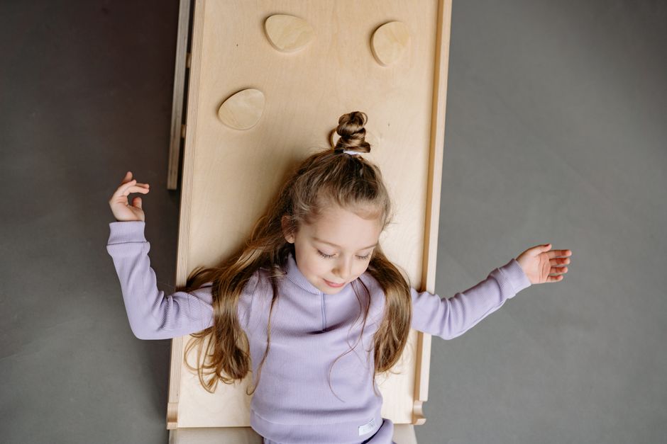 Top view of a girl in a purple sweater lying relaxed on a wooden slide indoors.