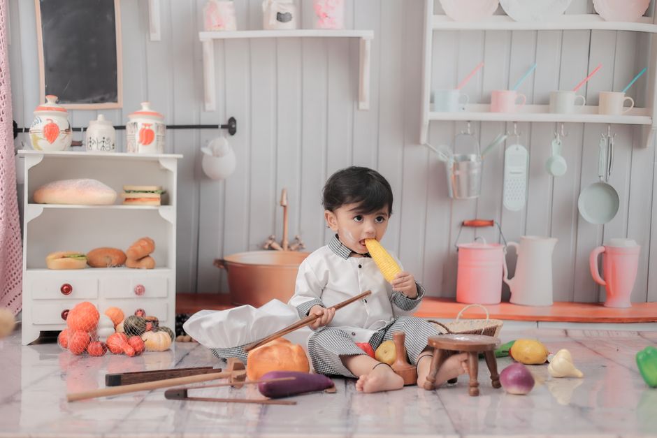 Cute child in chef outfit playing with toy food in a play kitchen environment.