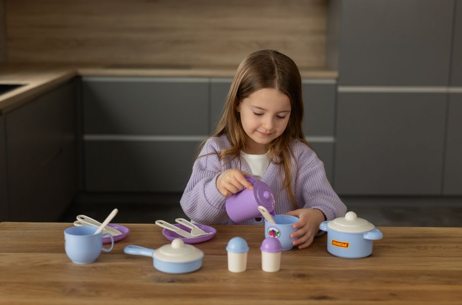 Child enjoying playtime with a colorful toy tea set on a wooden table at home.