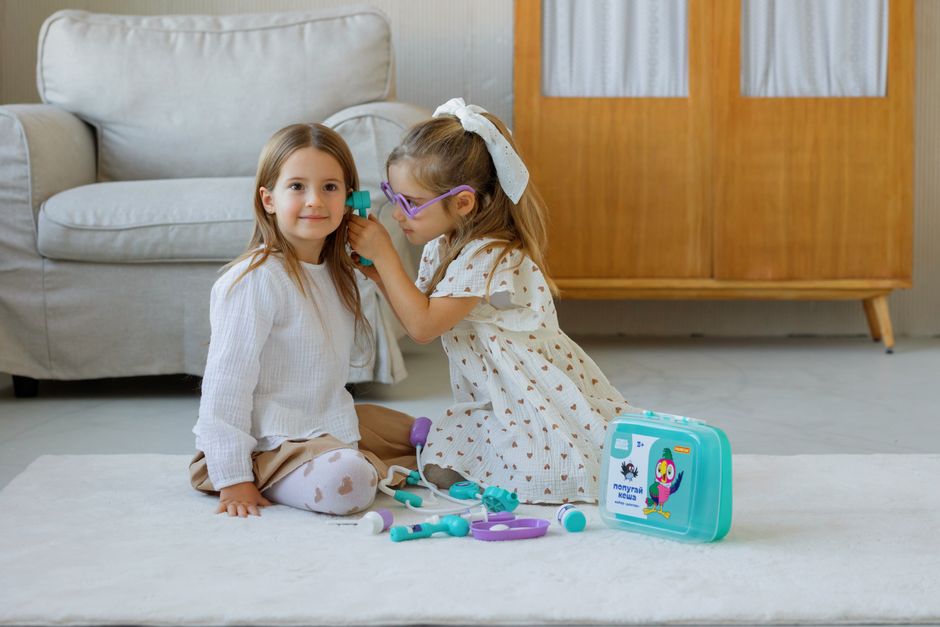 Two young girls play doctor with a toy medical kit in a cozy room setting.