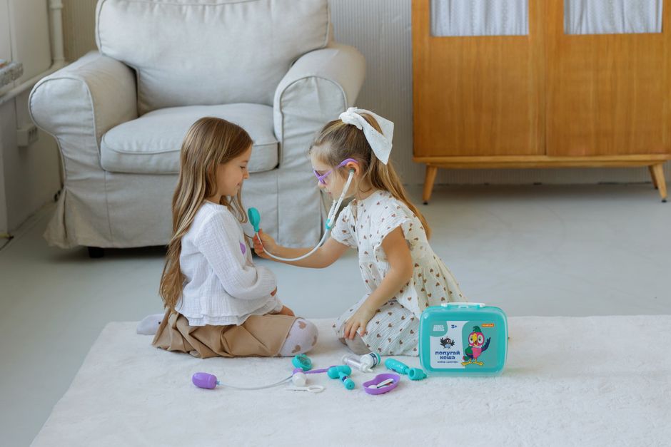 Two young girls play doctor with a toy medical kit in a cozy living room setting.