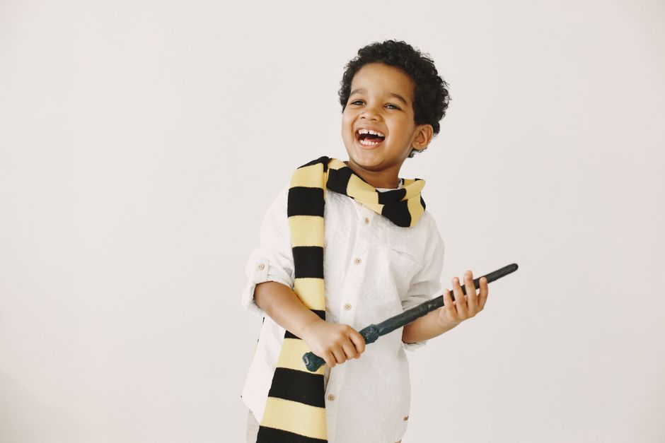 Adorable child smiling joyfully holding a magic wand while wearing a striped scarf.