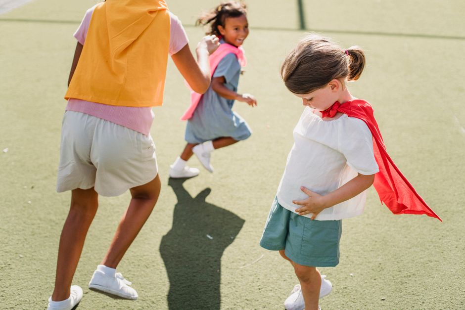 Children dressed as superheroes playing and running outdoors on a sunny day.