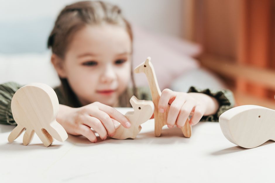 Young girl engages creatively with wooden animal toys in a playroom setting.