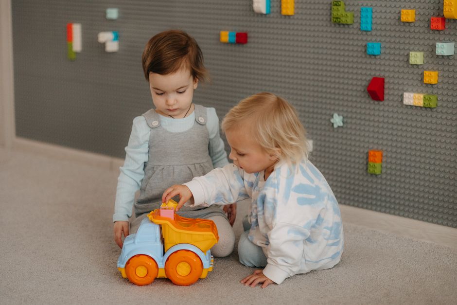 Two young children playing with a toy truck in a cozy indoor setting, exploring together.