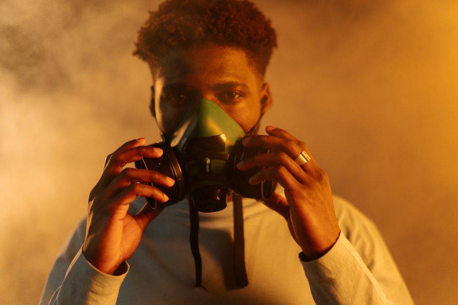 An adult man wearing a gas mask amidst smoke, emphasizing air pollution and protection themes.