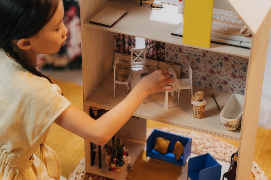 A young girl playing with a dollhouse indoors, showcasing childhood imagination and playtime.