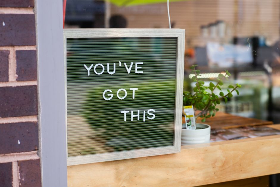 Vibrant image of a motivational sign 'YOU'VE GOT THIS' displayed in a cafe window next to a potted plant.