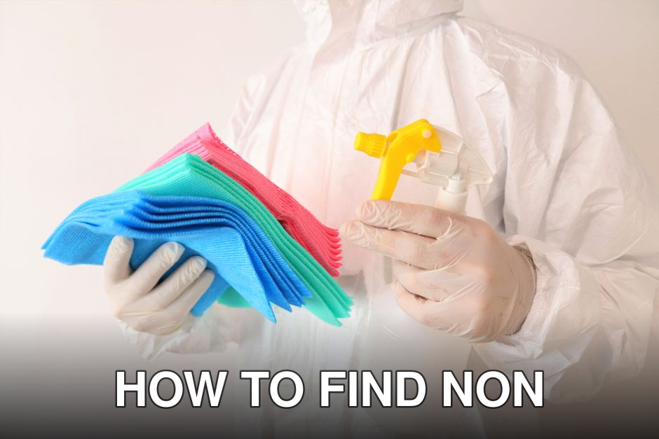Individual in PPE holds cleaning cloths and spray bottle, ensuring hygiene and safety.
