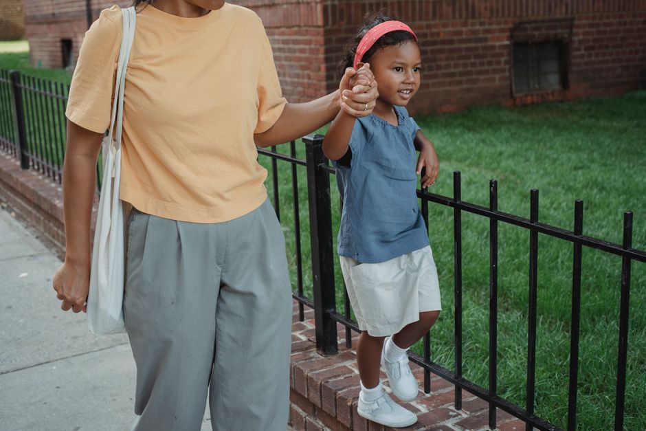 High angle of Asian smiling daughter holding hand of mother while strolling together near fence