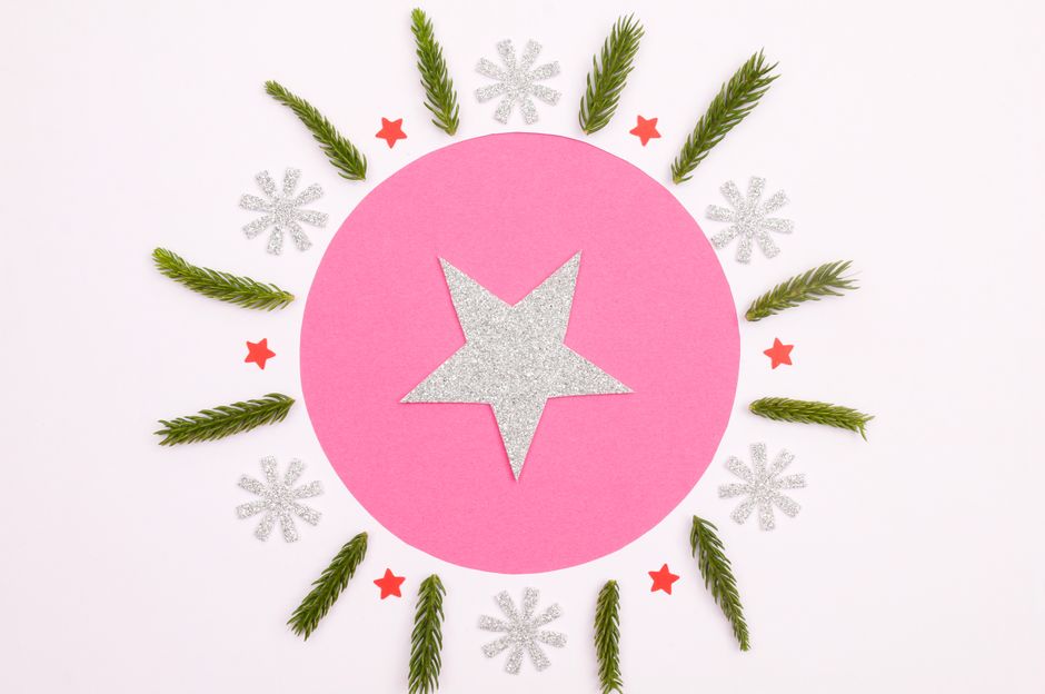 Creative Christmas card design with glitter star and pine leaves on pink background.