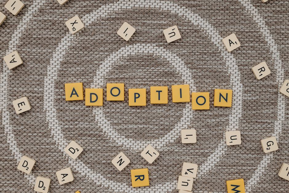 Top view of scrabble letters spelling 'adoption' surrounded by random letters on a patterned surface.