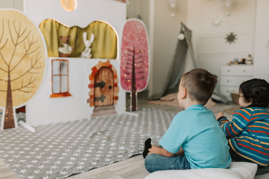 Two children watching a charming indoor puppet show with colorful backdrop.
