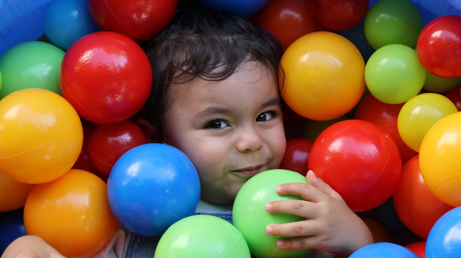 Adorable child smiling and playing in a vibrant ball pit indoors.