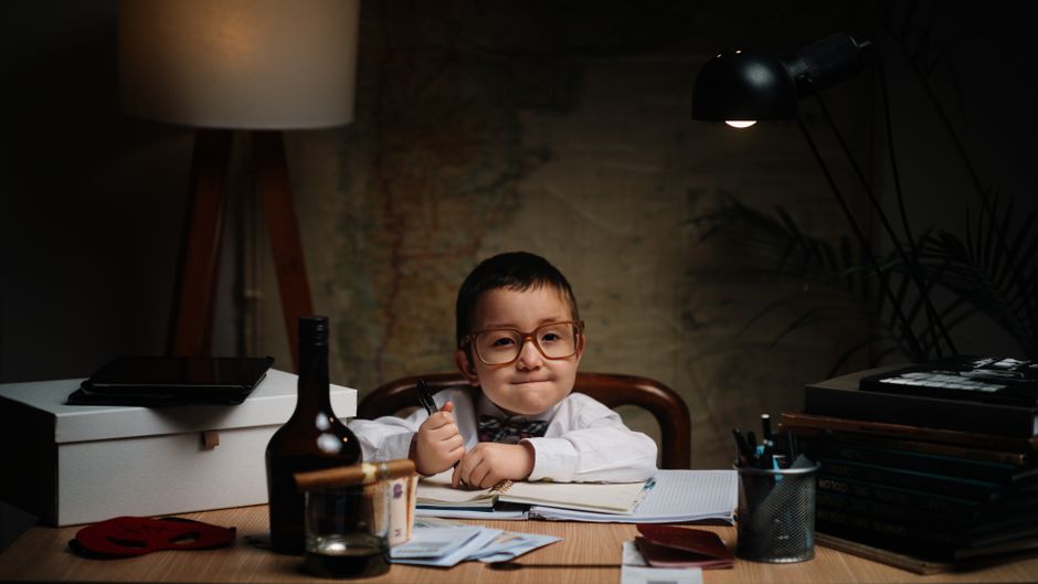 Cute boy in oversized glasses sitting at a desk, playfully imitating a business professional.