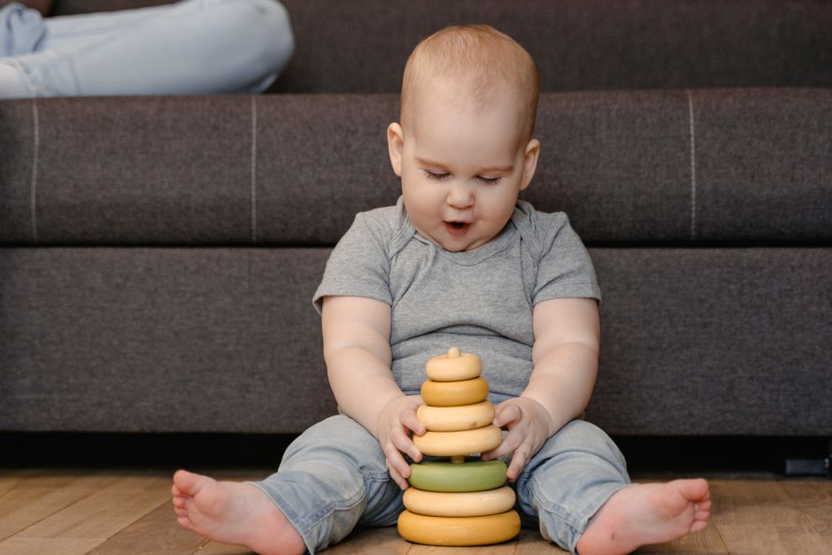 Adorable baby sitting on the floor, engaged with a colorful stacking toy in a cozy indoor setting.