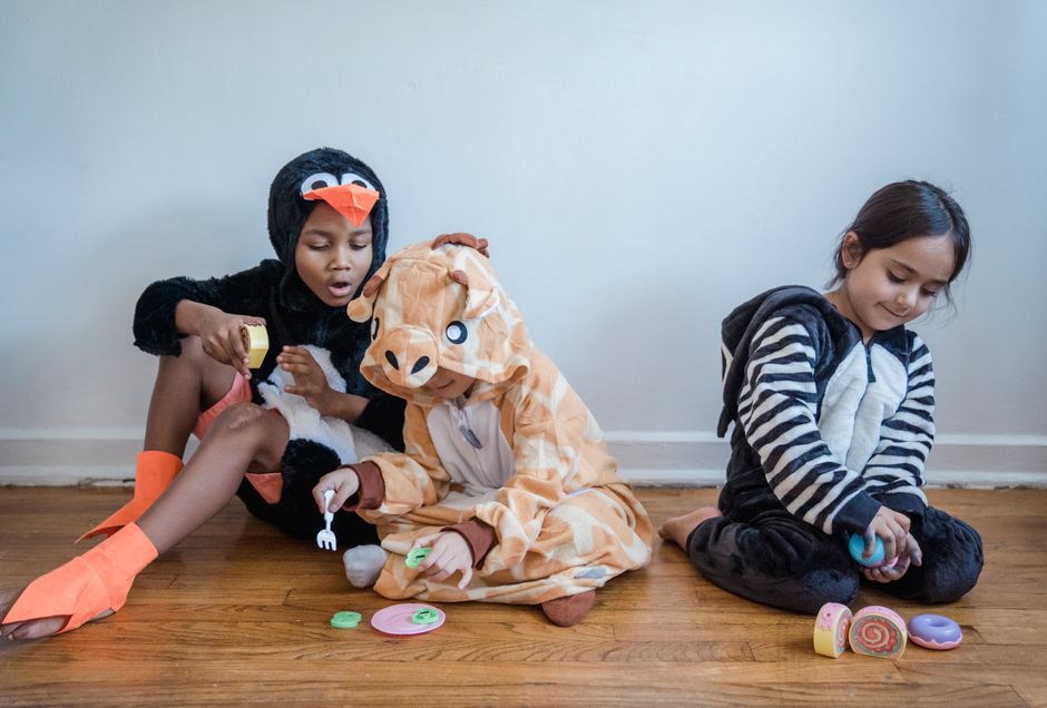 Children in fun animal costumes sitting and playing with toys on a wooden floor, indoors.