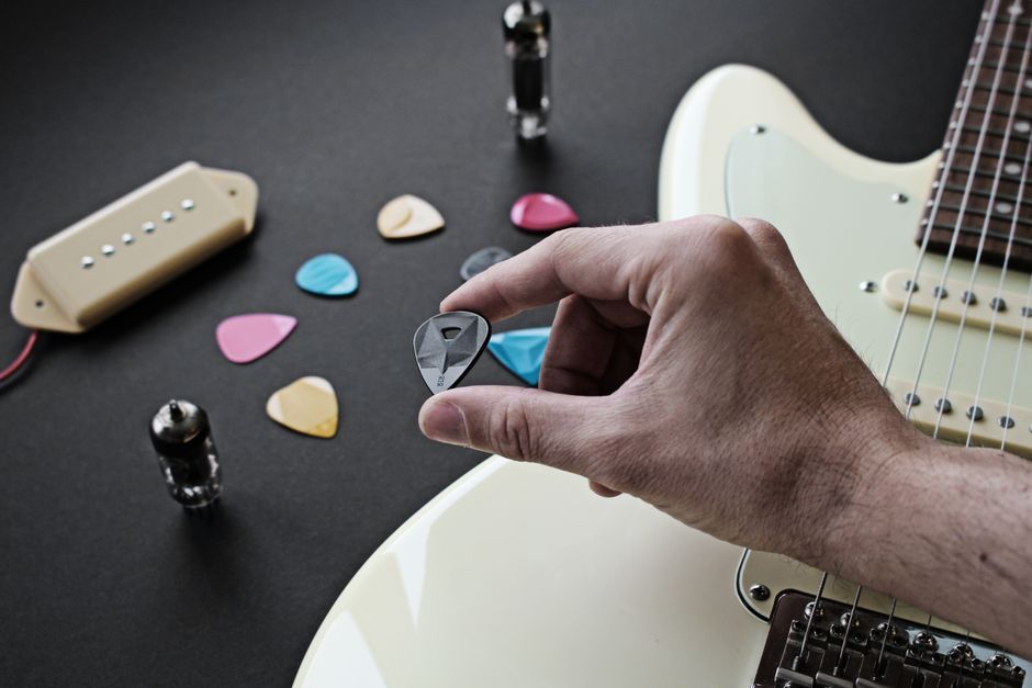 Close-up of a hand holding a plectrum with colorful guitar picks and an electric guitar, highlighting musical variety.