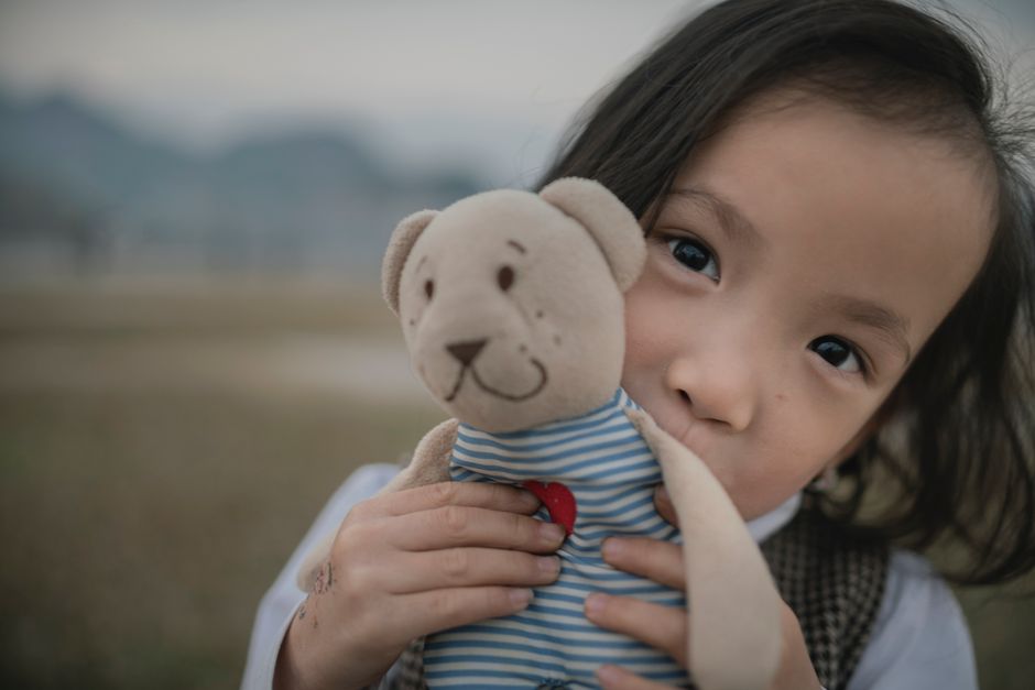 Adorable child embracing a teddy bear with a heart outdoors in a serene setting.