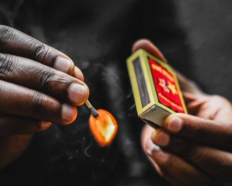 A detailed close-up of hands igniting a matchstick, showcasing the flame and action.