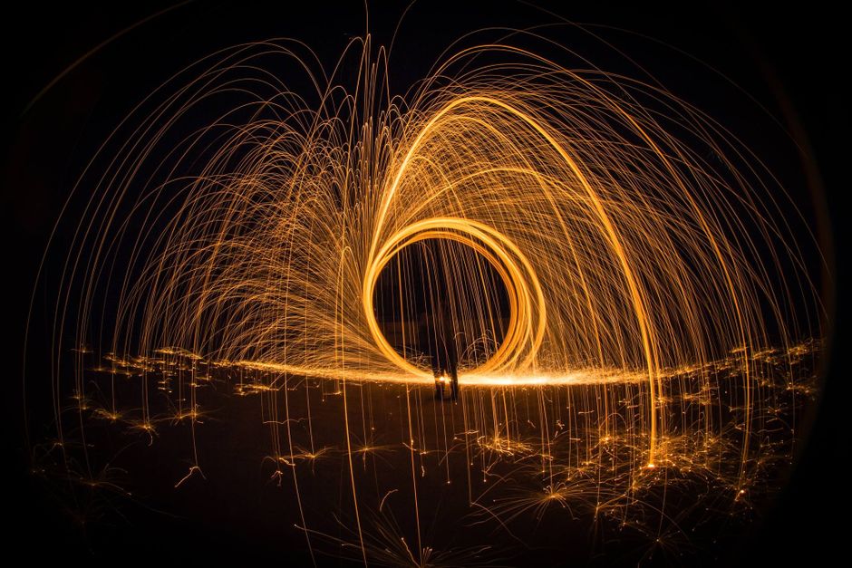 Stunning long exposure shot of steel wool light painting creating bright, glowing arcs in the night.