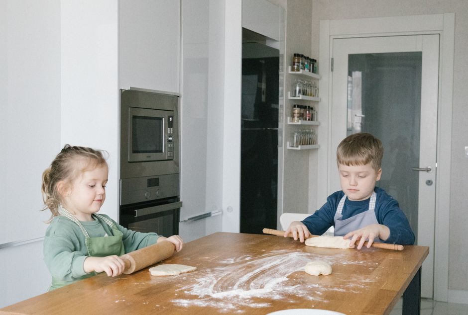 Two children baking at home in a modern Istanbul kitchen, rolling dough with focused expressions.